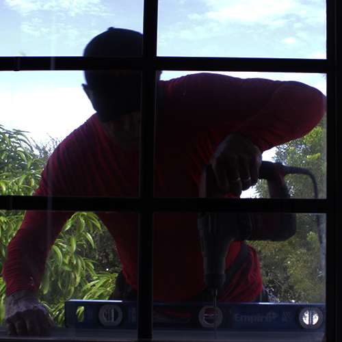 shutter installer seen through window while he is drilling a hole.