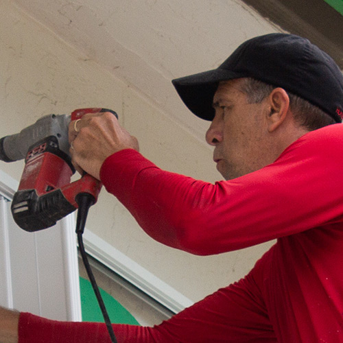 shutter installer drilling anchor holes in the outside wall.